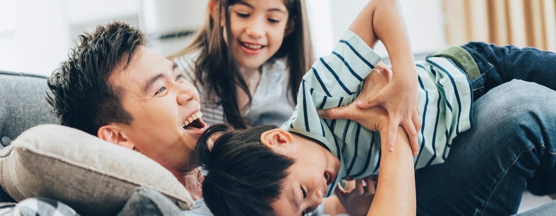 father plays on a couch with his young children